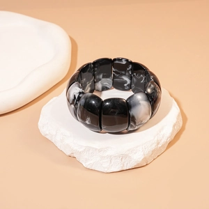 Detailed view of wide black and white marble resin bracelet on a stone pedestal