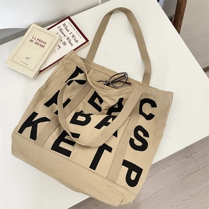 Flat lay of khaki canvas tote bag with black letter print and lifestyle props