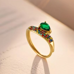 Dettaglio macro di anello dorato con zircone verde a goccia e pavé di pietre multicolore