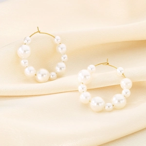 Close-up of gold U-shaped hoop earrings featuring elegant gradient white pearls on silk