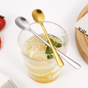 Polished gold and silver stainless steel long handle coffee spoons in a glass of lemonade