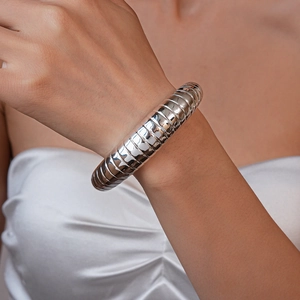 Macro shot of a silver polished segmented wide cuff bracelet on a white satin sleeve