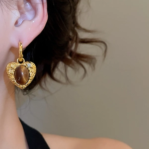 Close-up of model wearing heart-shaped gold earrings with brown tiger eye stone
