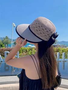 Detail of hollow woven straw sun hat featuring a large black bow and navy blue piping