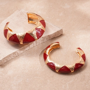 Macro detail of vintage gold-plated C-shape hoop earrings with red enamel geometric patterns