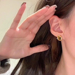 Detail of 18k gold-plated oval earrings with tiger eye stone and crystals on ear lobe
