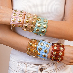 Close-up of chunky resin bangle bracelets with gold metal studs in six assorted colors