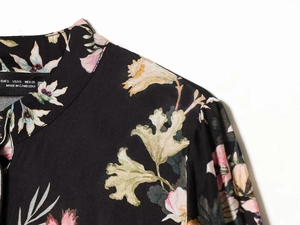 Détail du col et de l'épaule d'une robe chemise noire à fleurs avec étiquette de taille