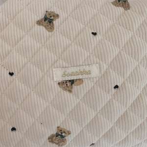 Detail of cream corduroy quilted pouch featuring a cute bear pattern and gold label
