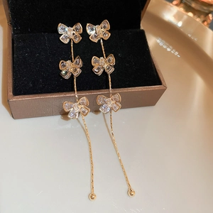 Détail de boucles d'oreilles pompons dorées avec trois papillons en zircon sur une boîte