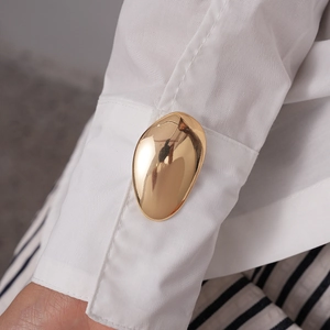 Detailed macro view of golden oval cufflinks on white shirt cuff with mirror finish
