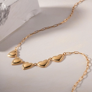 Detail of gold necklace featuring five heart pendants with beaded edges on a textured surface