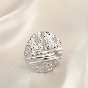 Macro detail of silver ring with hammered metal texture on silk fabric background