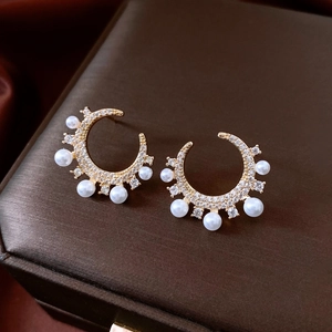 Detailed view of gold plated C-shaped pearl earrings with cubic zirconia on jewelry box