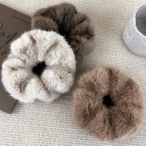 Plush faux fur scrunchies in beige and brown colors on a soft woven background