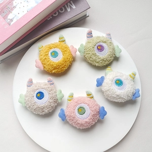 Plush monster brooches in five pastel colors with embroidered eyes on white tray
