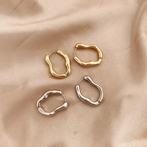 Irregular wavy hoop earrings in gold and silver metal finish on beige silk fabric