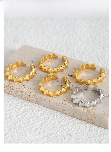 Close-up of gold and silver wavy stackable rings on a textured beige stone base