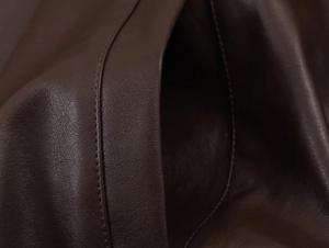 Detailed close-up of dark brown faux leather texture and precise stitching on the jacket