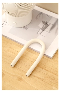 Macro detail of a flexible white S-shaped hook on a wooden desk with a minimalist setup
