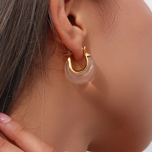 Close-up of elegant gold and transparent acrylic C-shaped hoop earrings on model