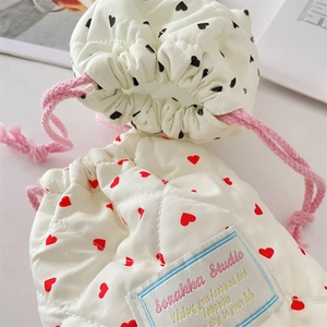 Close-up of quilted cream camera pouch with red heart patterns and pink drawstrings