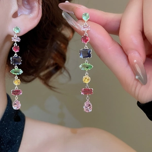 Close-up of dangling drop earrings with colorful zircon stones in geometric shapes