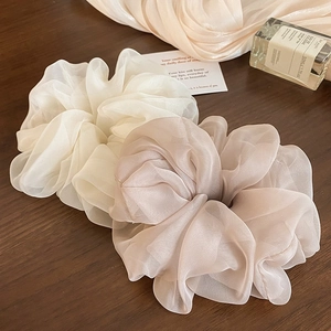 Detail of off-white and khaki mesh scrunchies on a wooden table with elegant accessories