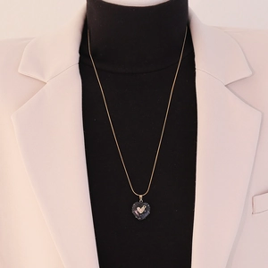 Close-up of a model wearing a heart pendant necklace with shimmering dark stone detail