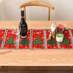 Close-up of red Christmas table runner with green pine tree pattern on wood table