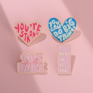 Macro detail of alloy enamel pins set with retro letter slogans on pink background