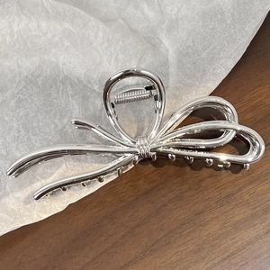Detailed view of a silver alloy bow hair claw clip placed on textured white paper