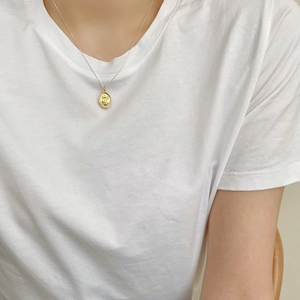 Detail of a gold smile face pendant on a silver chain worn by a model in a minimalist style