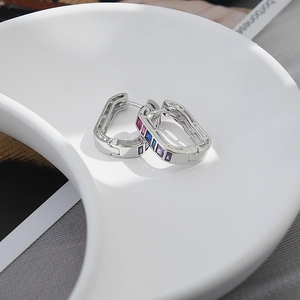 Close-up of luxury geometric silver earrings with colorful zircon stones on a ceramic tray