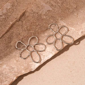 Detailed view of silver minimalist hollow metal flower earrings on a textured stone surface