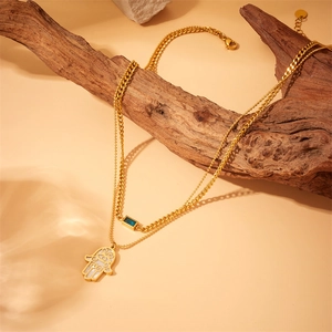 Detail of gold double-layered necklace with Hamsa Hand and blue stone on wood branch