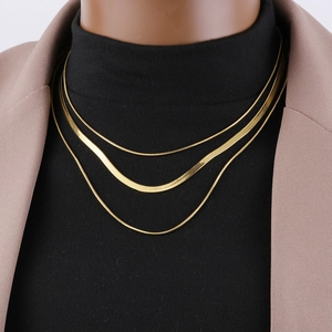 Close-up of triple-layered gold snake chain necklaces on a brown blazer and black knitwear