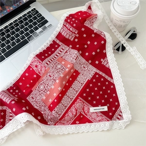 Detailed view of the 100% cotton floral red scarf with white lace edges on a white desk