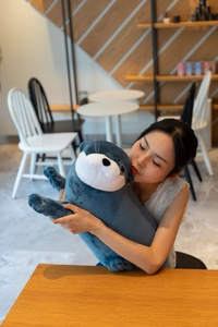 Detailed view of a soft blue otter plush doll held by a person in a cozy cafe setting