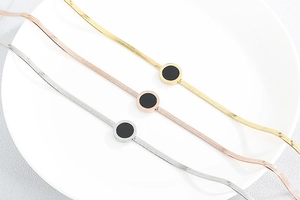 Detailed view of gold, silver, and rose gold snake chain bracelets with black round charms