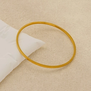 Minimalist gold-plated titanium steel round bangle on a textured beige sand background
