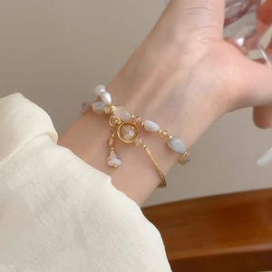 Dettaglio di bracciale rigido dorato con ciondolo e set di perle stratificate eleganti