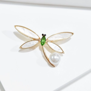 Macro detail of golden dragonfly brooch with crystal body and pearl tail accent