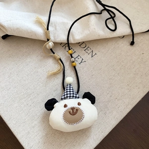 Close-up of a plush white bear pendant necklace with a check party hat and soft tassels