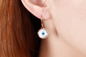Close-up of rose gold evil eye drop earring worn on ear with blue resin inlay