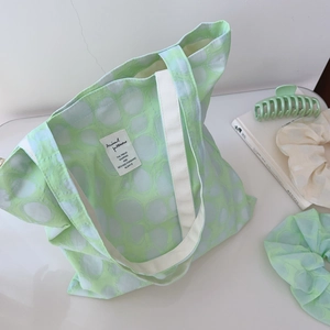 Detail view of mint green canvas tote with white polka dots and woven handles