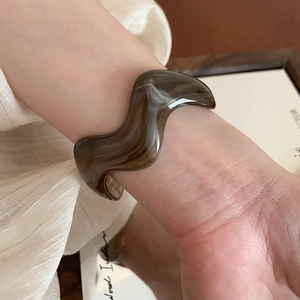 Detail of amber and beige marble wave acrylic cuff bracelet worn on a female wrist