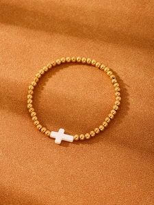 Close-up of golden beaded bracelet with white shell cross on warm orange fabric