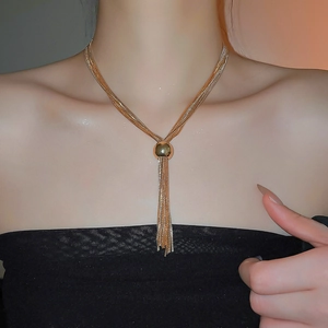 Dettaglio di collana multistrato dorata con sfera metallica e lungo pendente a nappa