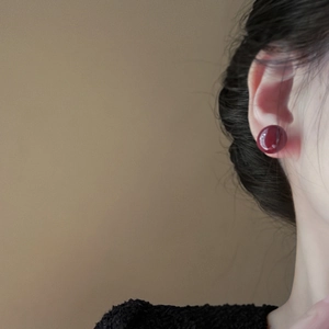 Elegant deep red round pearl stud earrings worn by a model in a minimalist style
